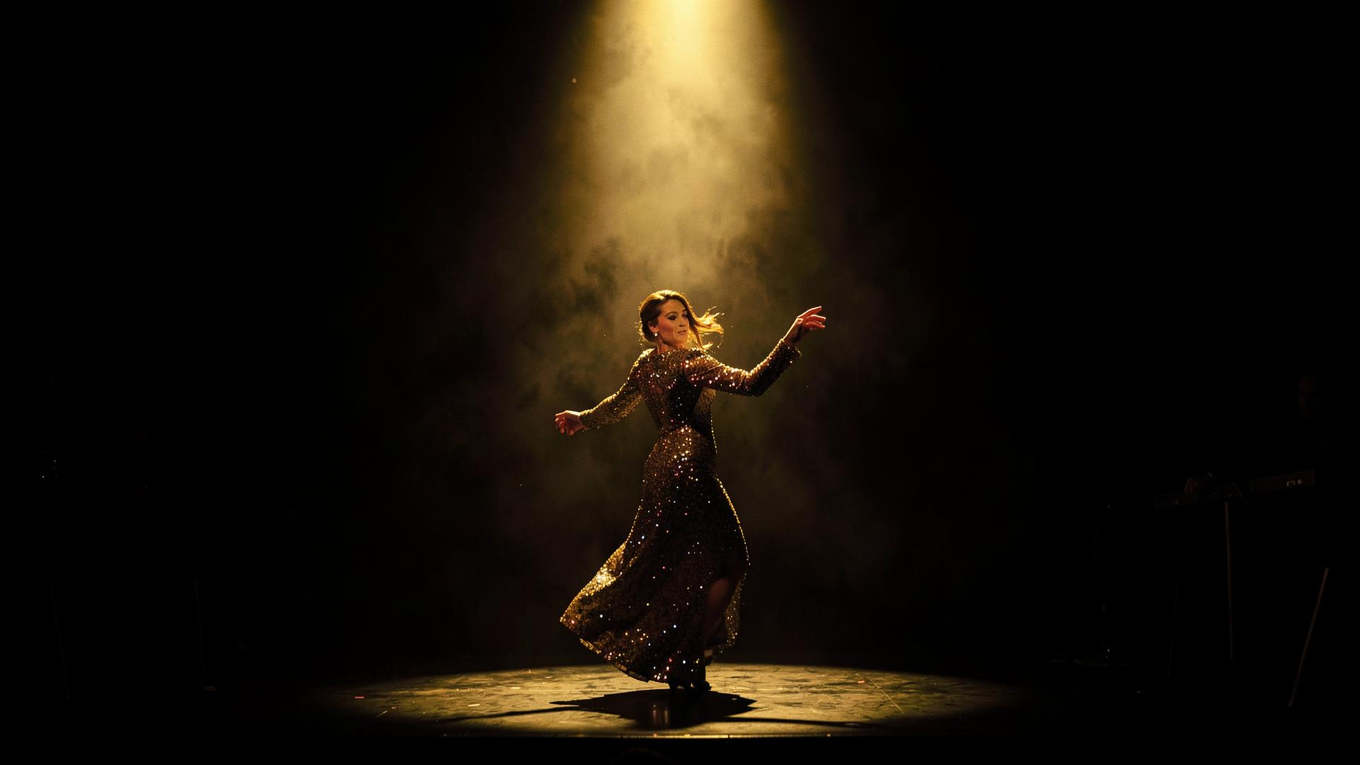 A sequined dancer mid-movement under a single golden spotlight on a dark stage